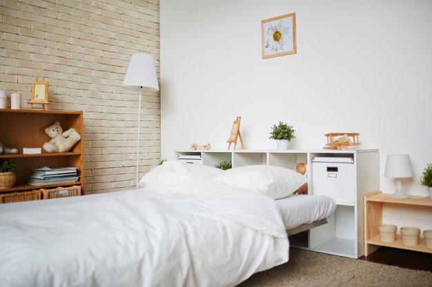 Habitación con una cama, una estantería marrón, otra estantería blanca, un par de lámparas y un cuadro en la pared.